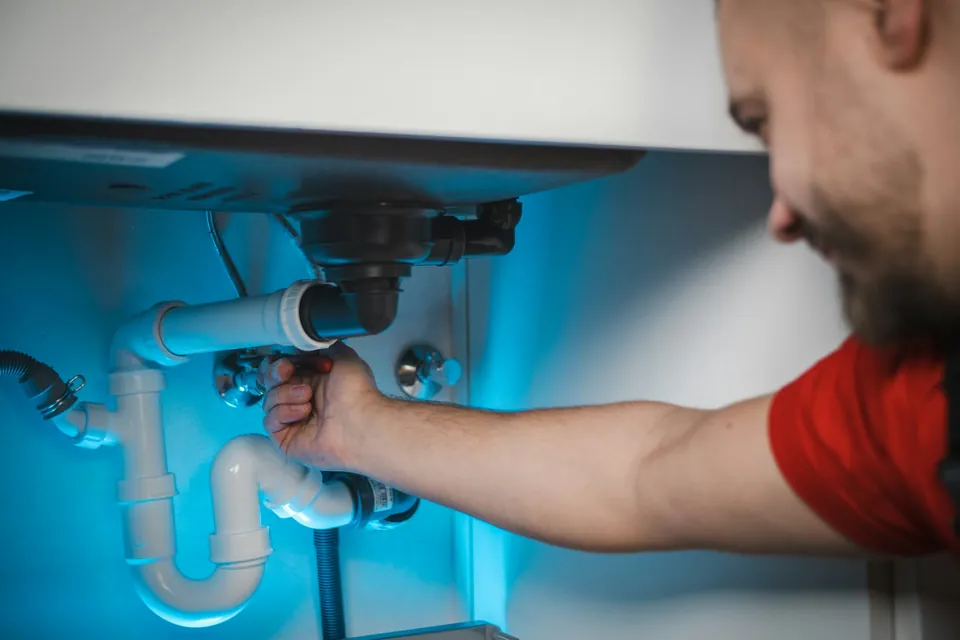 Gasfíter reparando las cañerías bajo un lavaplatos