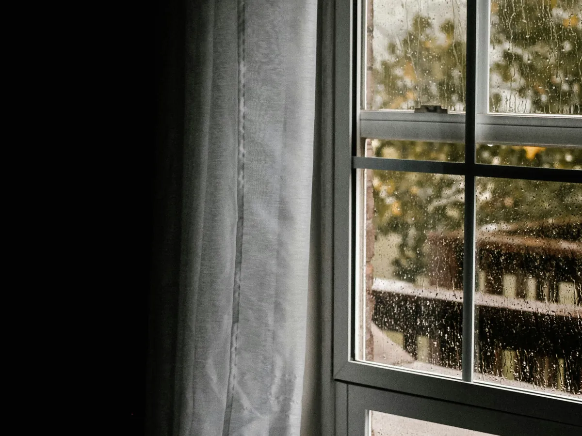 Ventana con gotas de lluvia en el vidrio vista desde una pieza oscura